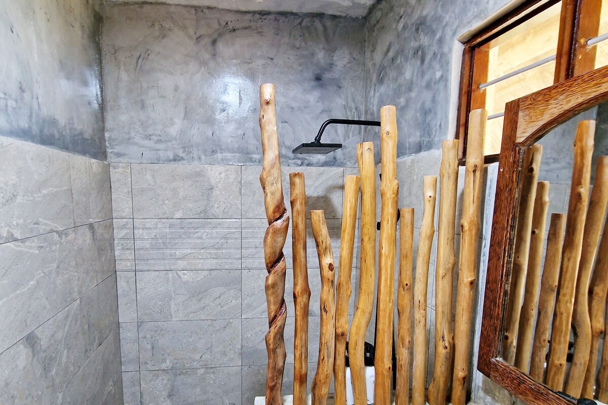 Un baño con pared de mármol, cabina de ducha con listones de madera y lavamanos blanco con grifo negro.