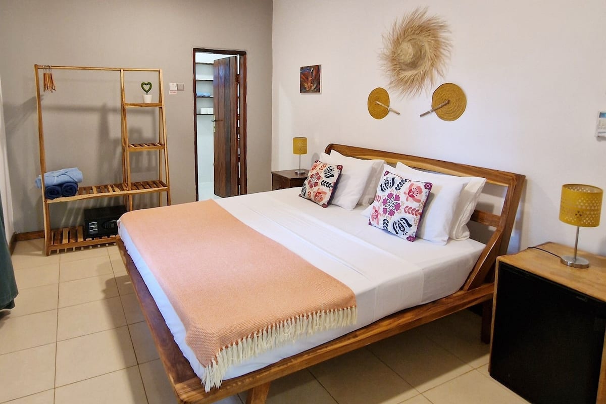 A neatly arranged bedroom with a wooden bed, a wardrobe, a small table with a lamp, and a decorative wall piece.