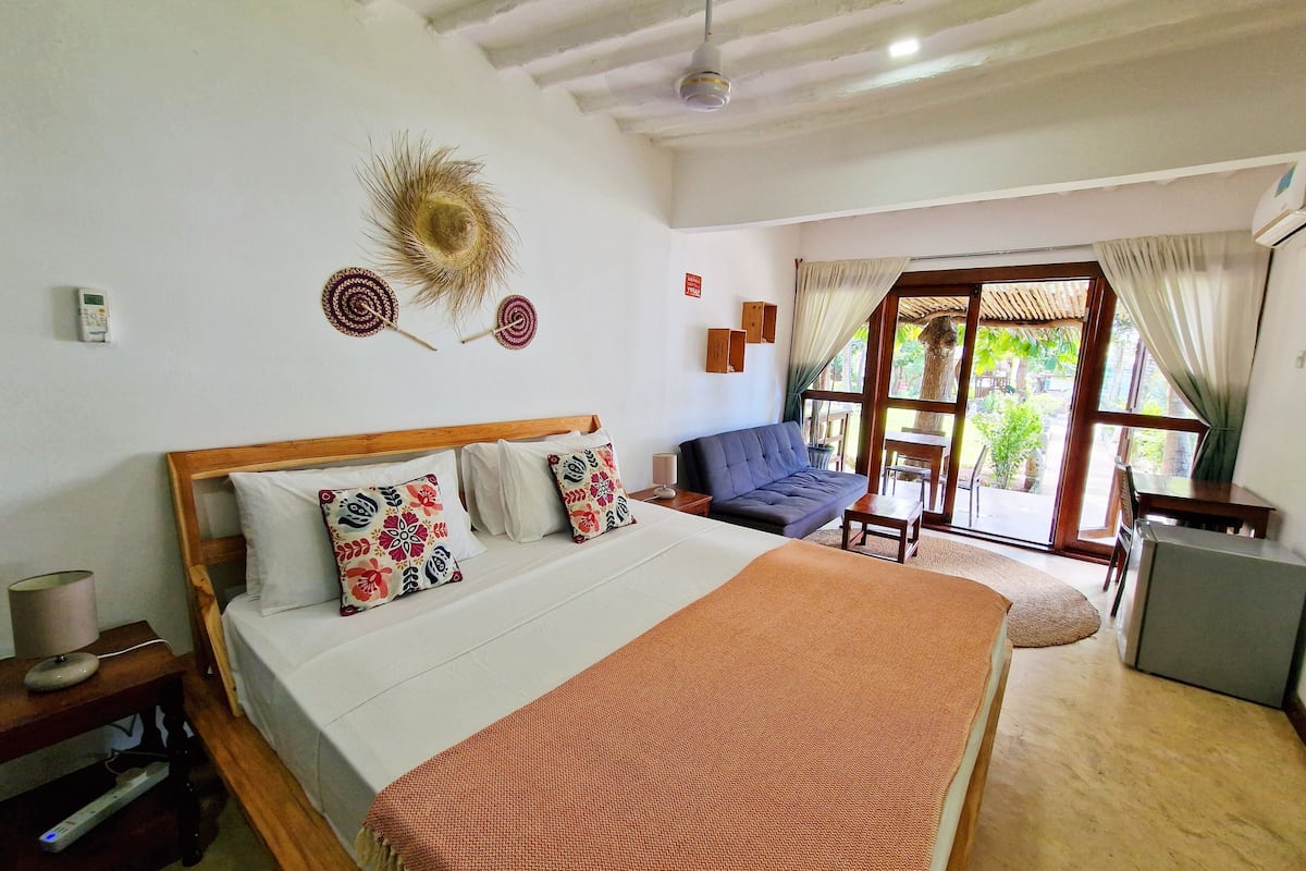 A bedroom with a bed, bedside tables, a sofa, and a view of the outdoors.