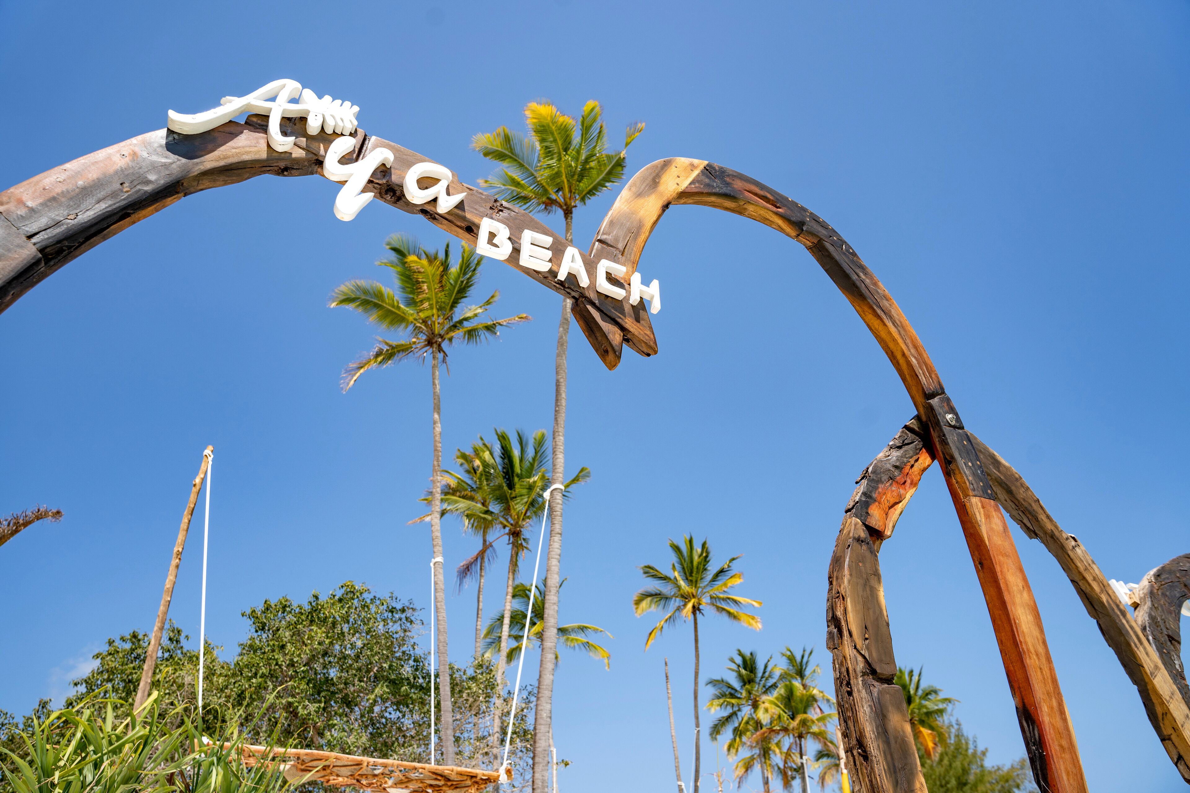 Ein hölzerner Bogen mit der Aufschrift "Caya Beach", umgeben von Palmen.