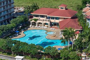 A large swimming pool with multiple sections, surrounded by lounge chairs and palm trees. - Jomtien Beach Condominium (Pattaya)