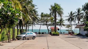 A coastal road with a parked car, palm trees, and a building with a red roof. - Jomtien Beach Condominium (Pattaya)