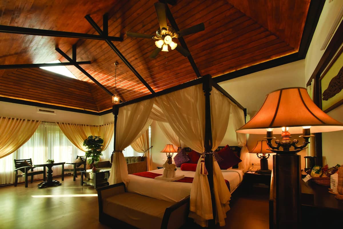 A room with a four-poster bed, a sitting area with a table and chairs, and a ceiling fan.
