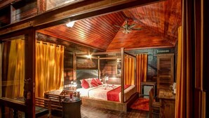 A cozy log cabin bedroom with a four-poster bed, a small table, and a fireplace. - Wild Planet Resort (Nilambur)