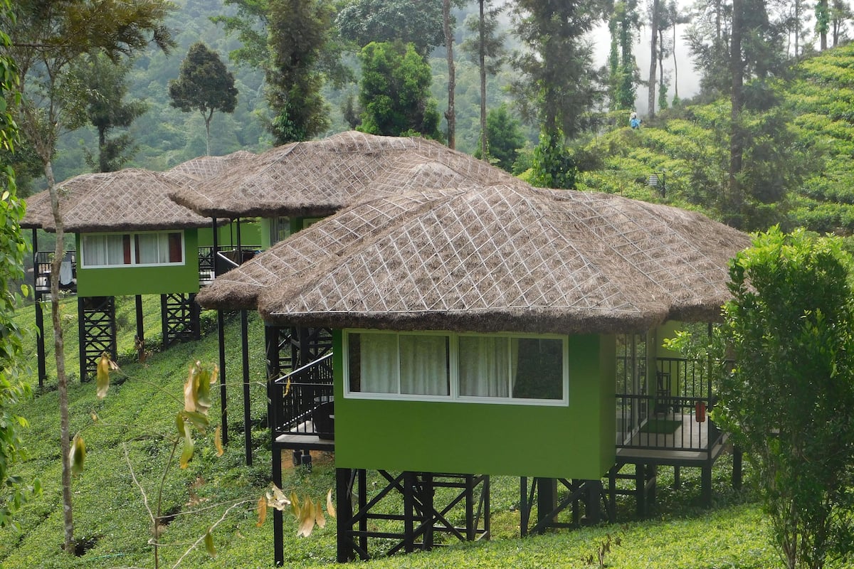 A row of green-roofed cottages with thatched roofs, wooden staircases, and a lush green landscape.