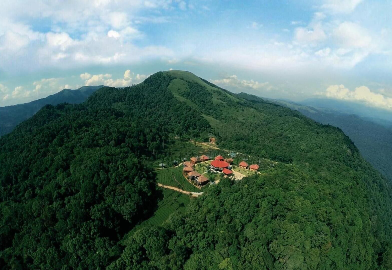Vista aérea de una zona montañosa con un conjunto de edificios de tejados rojos rodeados de un bosque verde denso.