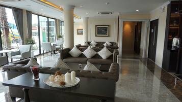 A modern hotel lobby with a seating area featuring a sofa and armchairs, a coffee table with snacks and candles, and large windows offering a view of the outside.
