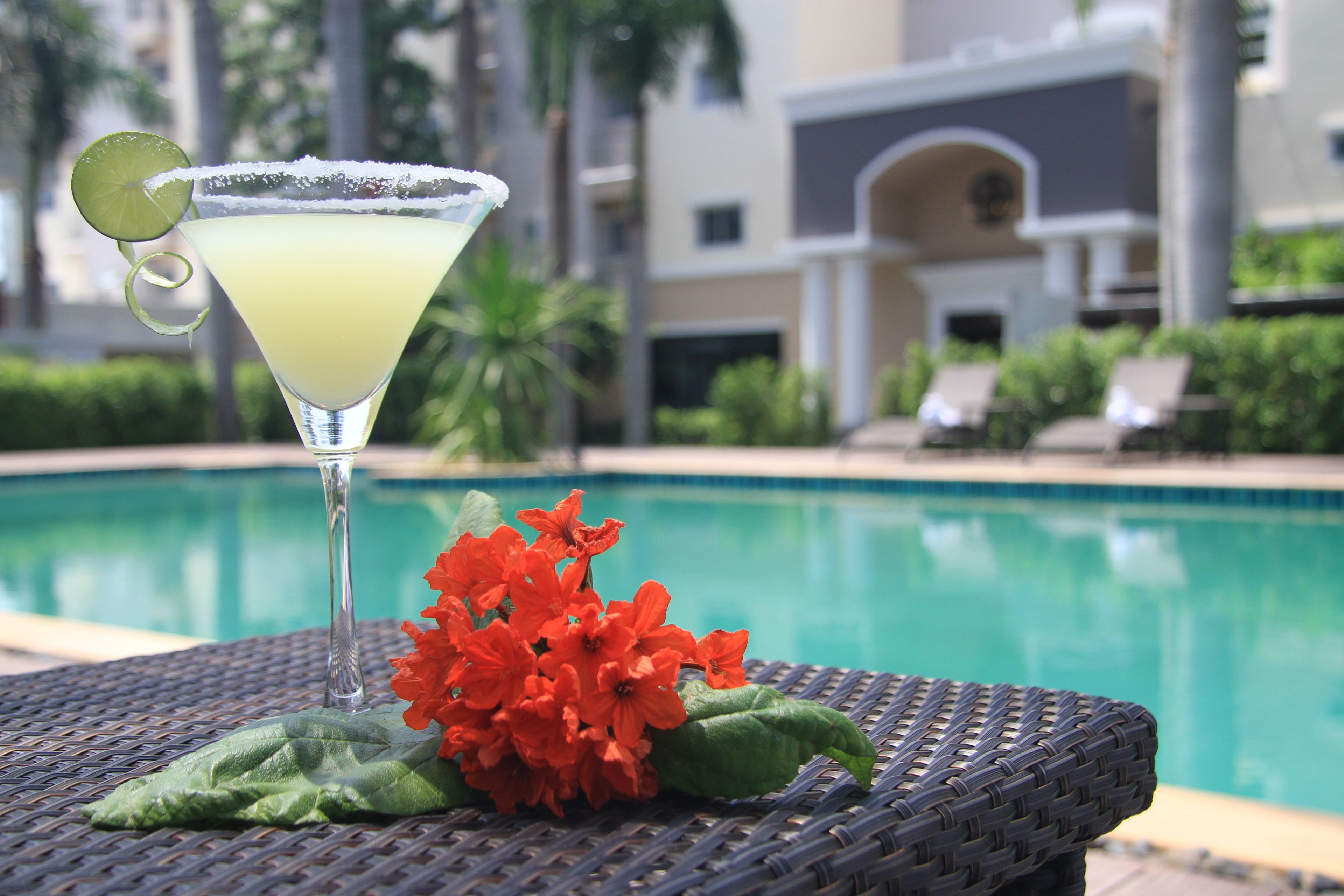 A cocktail with a lime garnish and a salted rim, placed on a wicker table with a pool in the background.