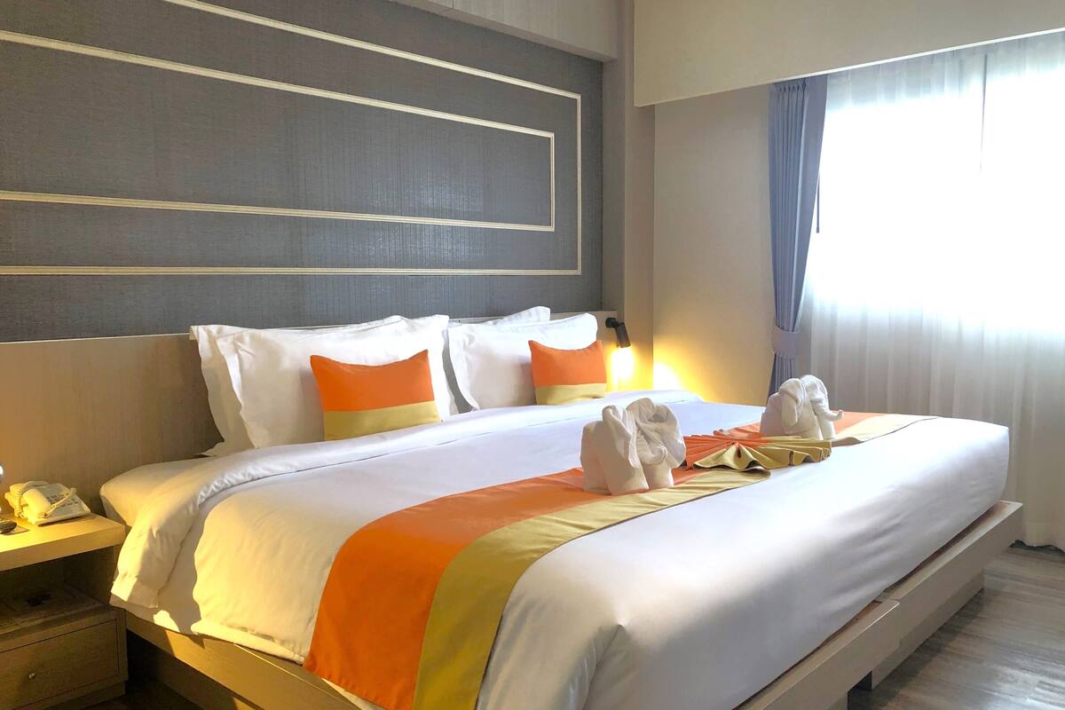 A hotel room with a neatly made bed, a bedside table with a lamp, and a window with curtains.