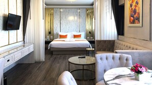 A hotel room with a bed, a seating area with a table and chairs, a TV mounted on the wall, and a painting on the wall. - The Green View Hotel (Bang Sao Thong)