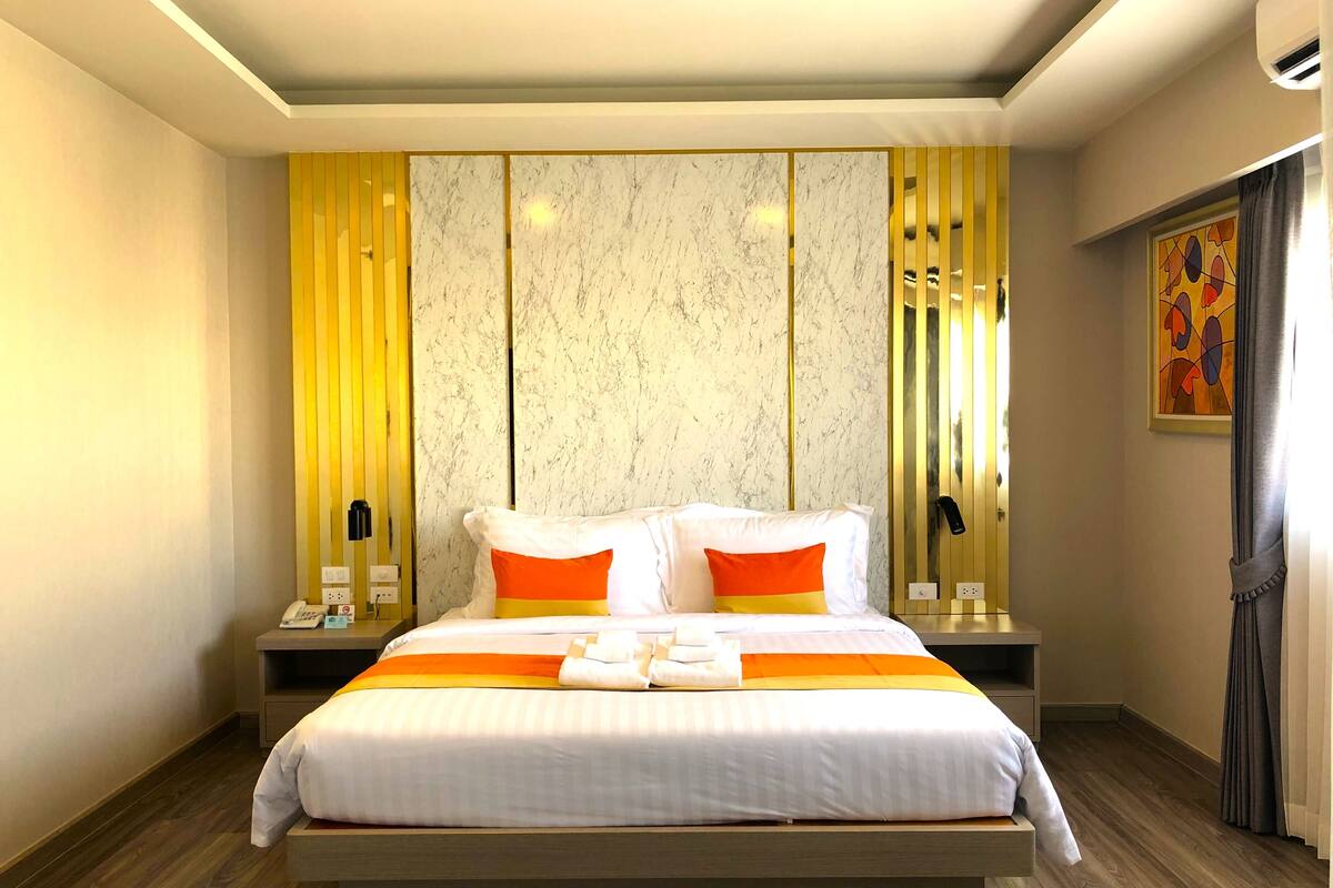 A hotel room with a large bed, a nightstand, a telephone, and a wall-mounted air conditioner.