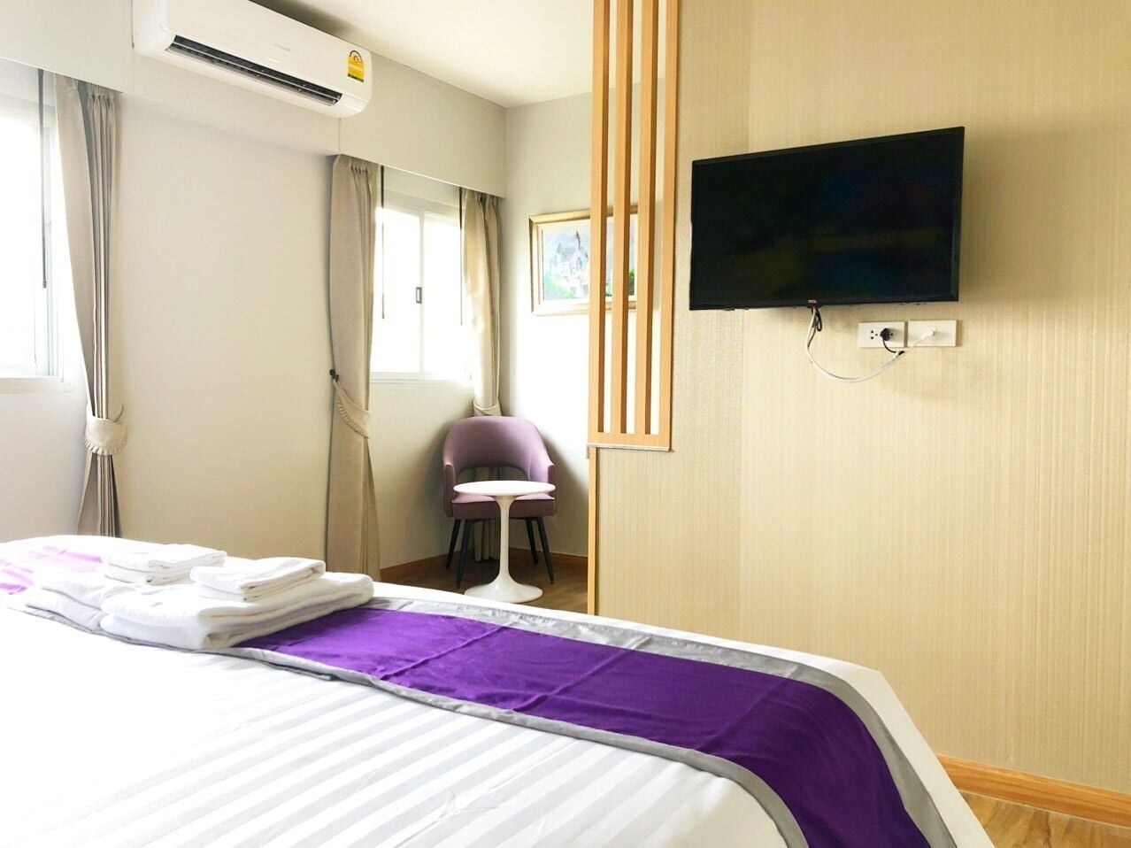 Une chambre d’hôtel avec un lit, un téléviseur fixé au mur, une chaise et une fenêtre avec des rideaux.