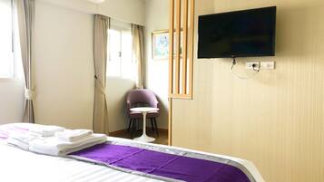 Une chambre d’hôtel avec un lit, un téléviseur fixé au mur, une chaise et une fenêtre avec des rideaux.