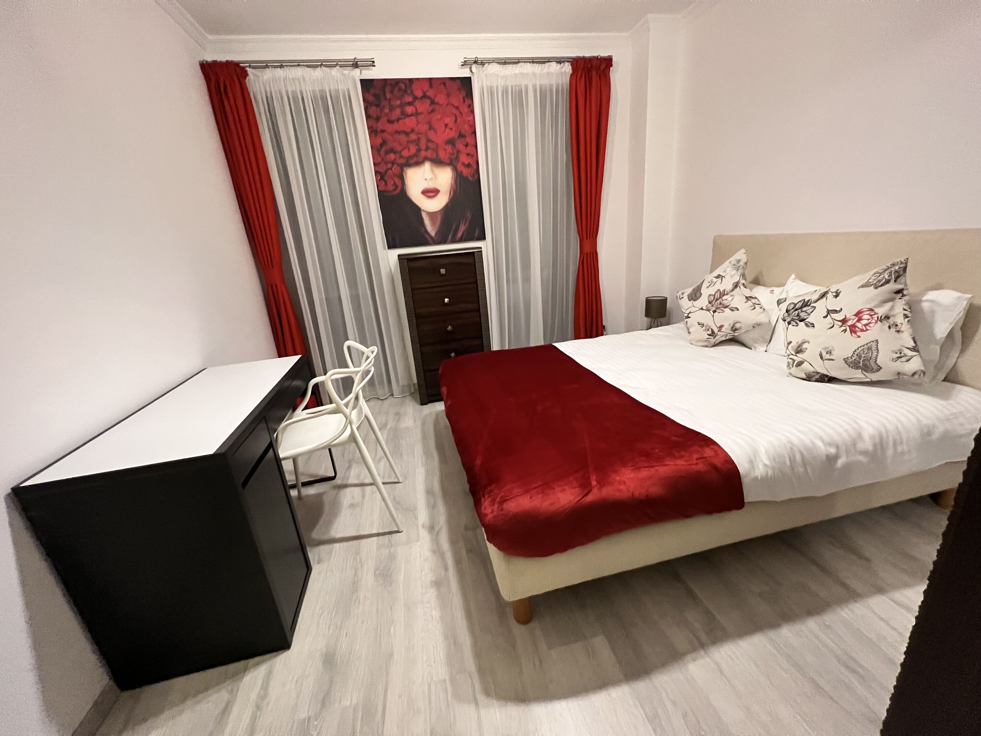 A bedroom with a bed, a desk, and a chair. There is a window with curtains.