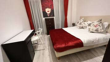 A bedroom with a bed, a desk, and a chair. There is a window with curtains.