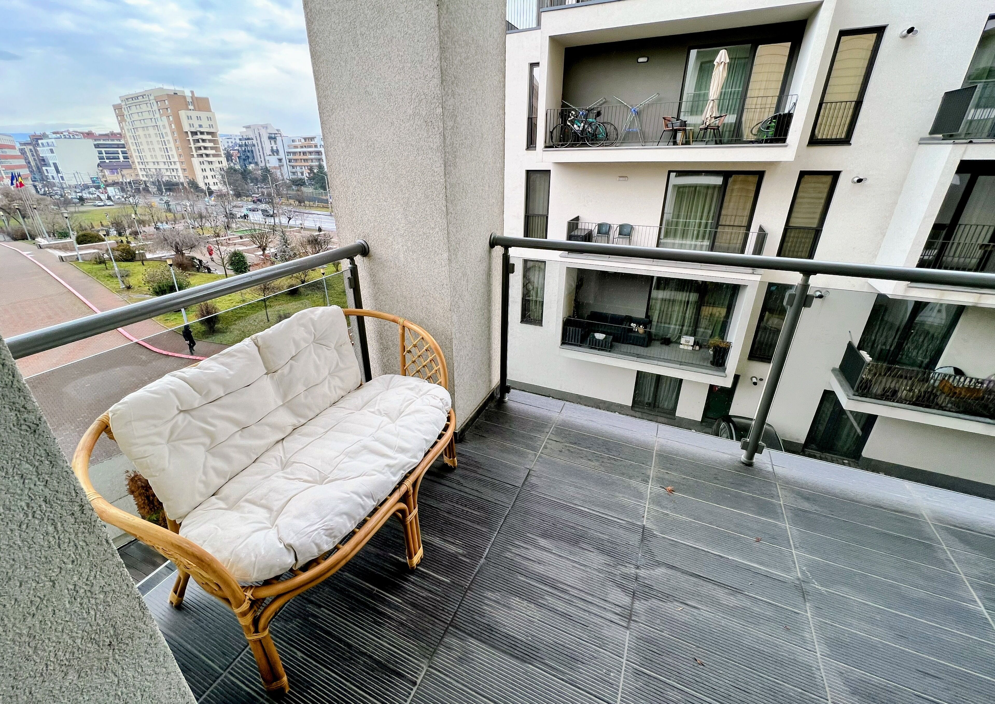 A balcony with a wicker sofa, a railing, and a view of a cityscape.
