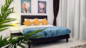 Quarto com uma cama, almofadas amarelas, colcha azul e duas obras de arte florais na parede.