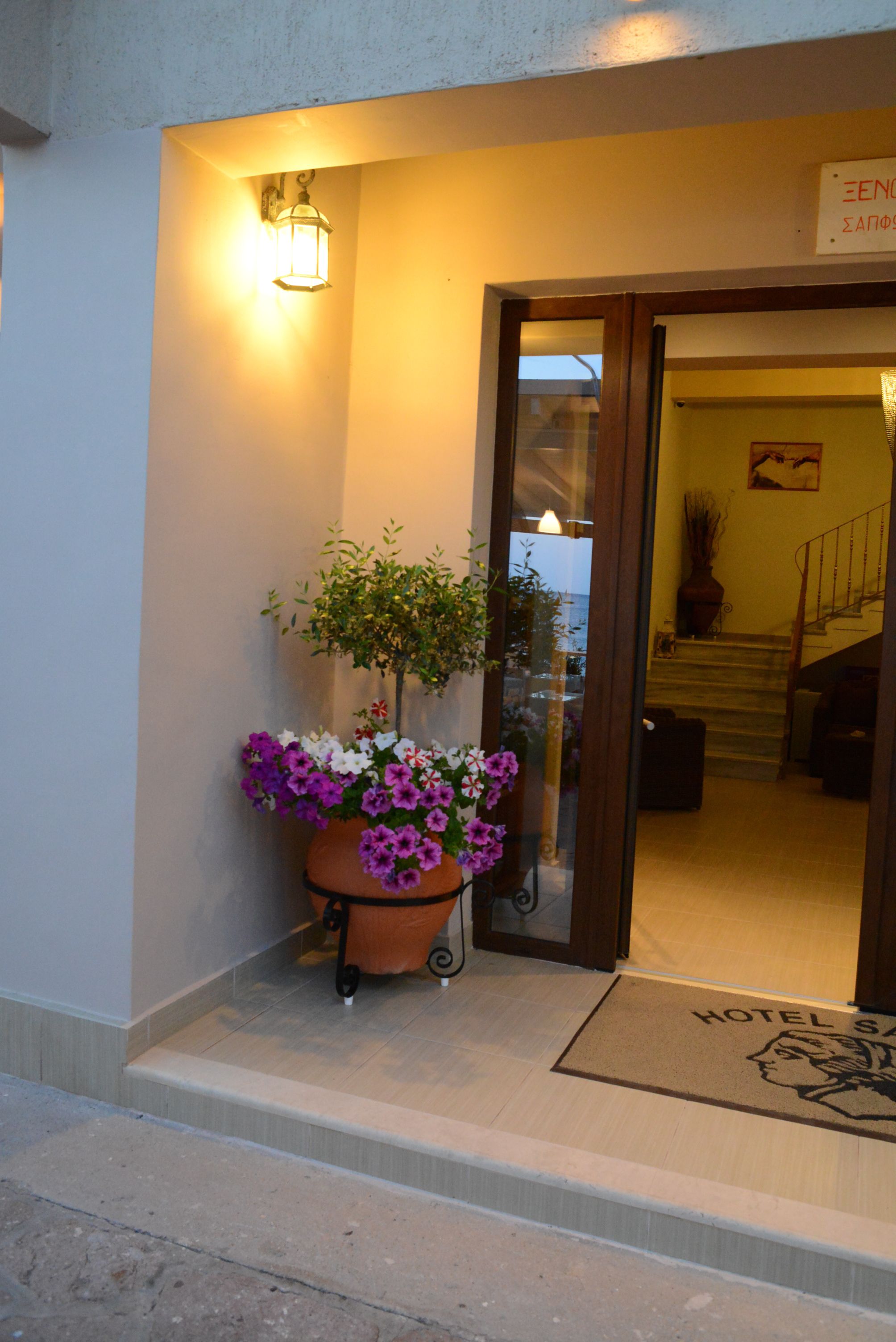 Entrada de hotel com planta em vaso, tapete e escadaria que leva para dentro.