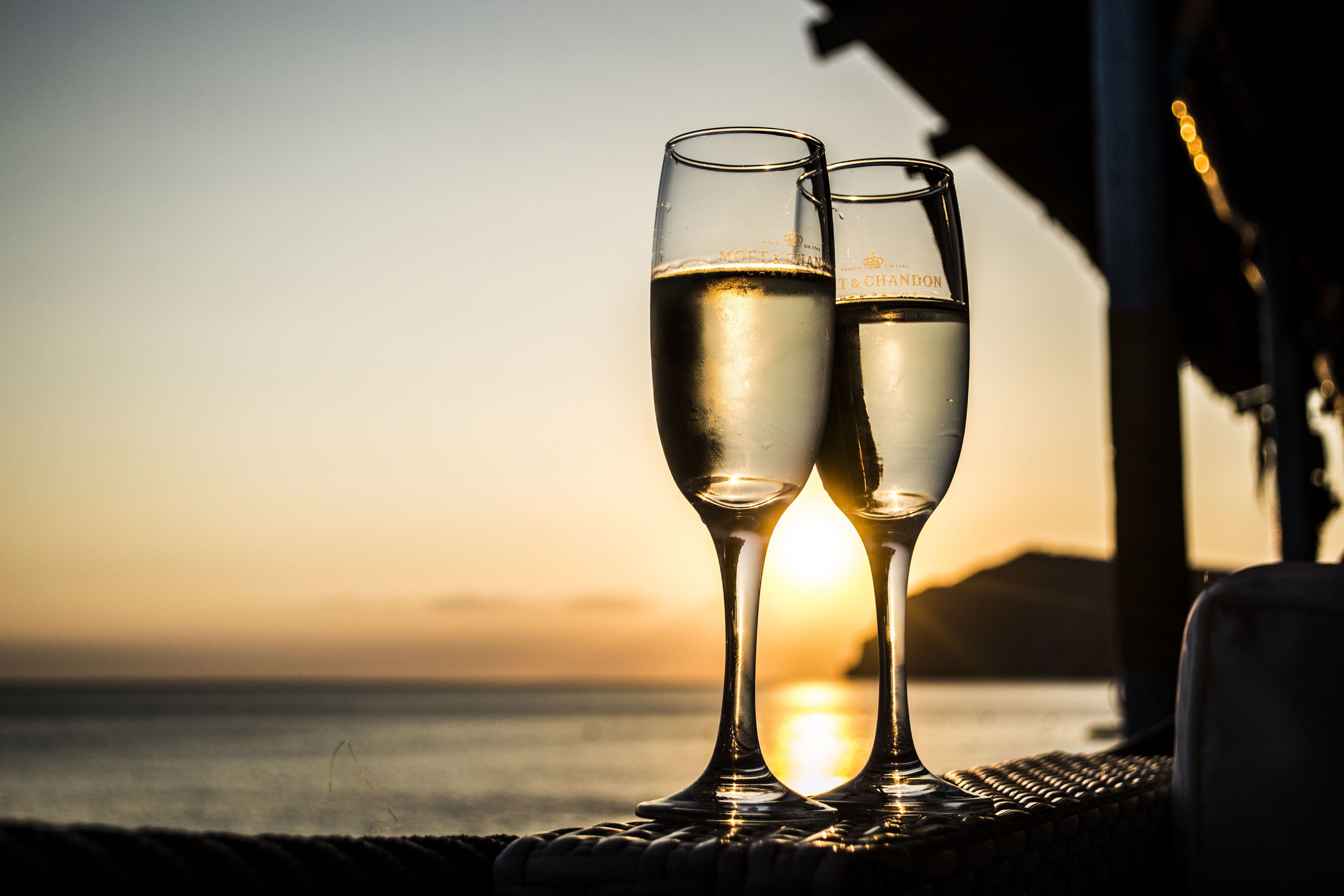 Two champagne glasses on a woven surface with a sunset in the background.