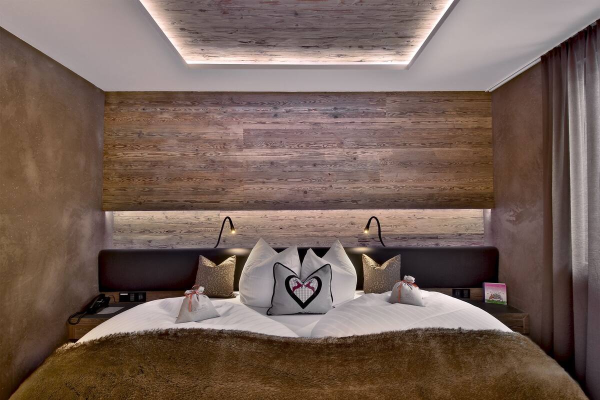 A modern bedroom with a wooden ceiling, a large bed with white bedding, and a heart-shaped pillow.