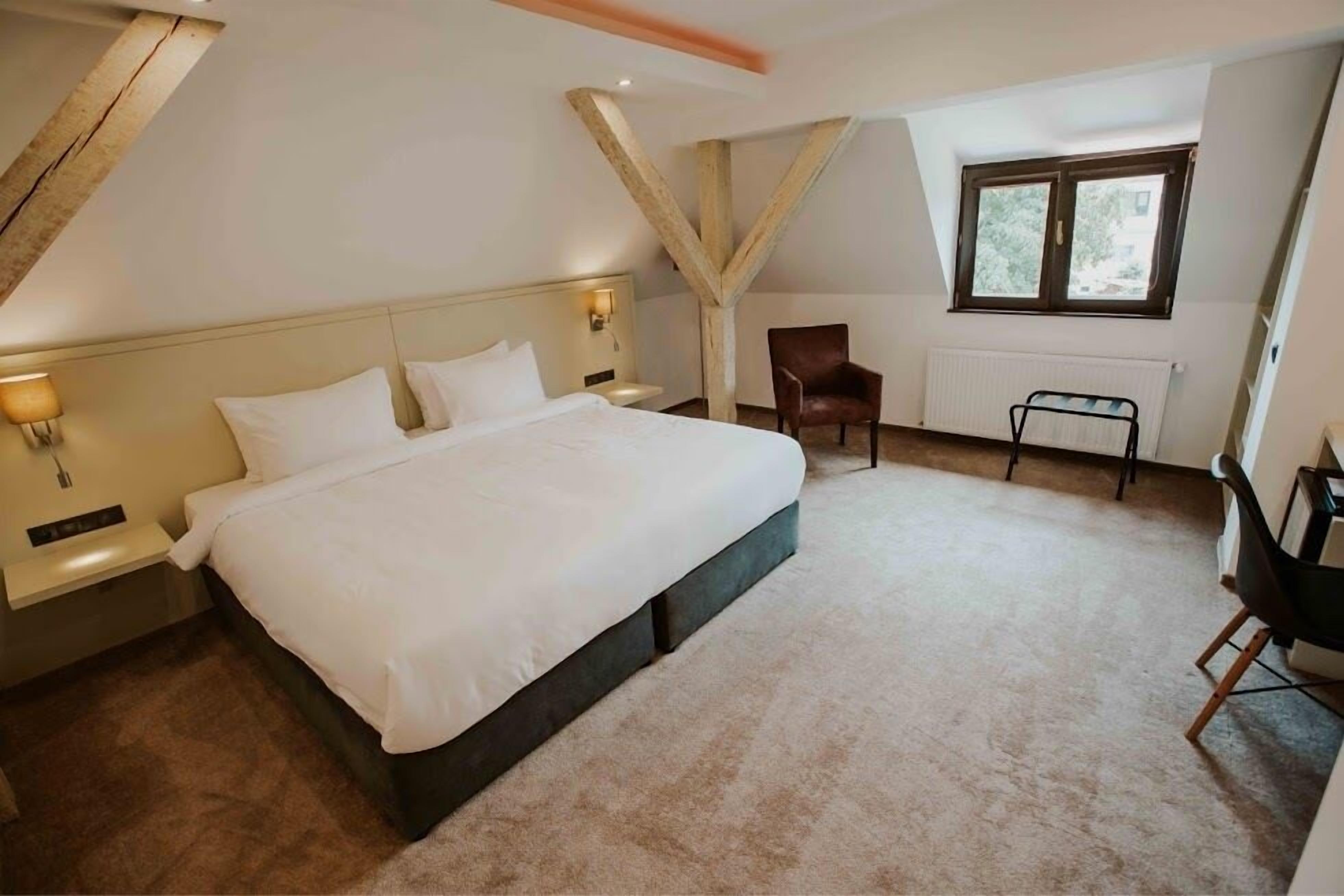 Une chambre à coucher avec un grand lit, une chaise, une table et une fenêtre.