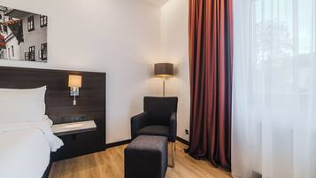 A hotel room with a bed, a desk, a chair, a lamp, and a window with curtains.