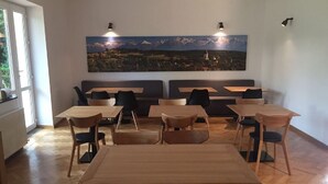A dining area with wooden tables and chairs, a large painting of a mountain landscape on the wall, and a window providing natural light. - Hotel Republique (Sibiu)