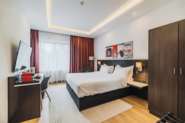 A modern hotel room with a large bed, a desk with a computer, a wardrobe, and a painting on the wall. - Hotel Republique (Sibiu)