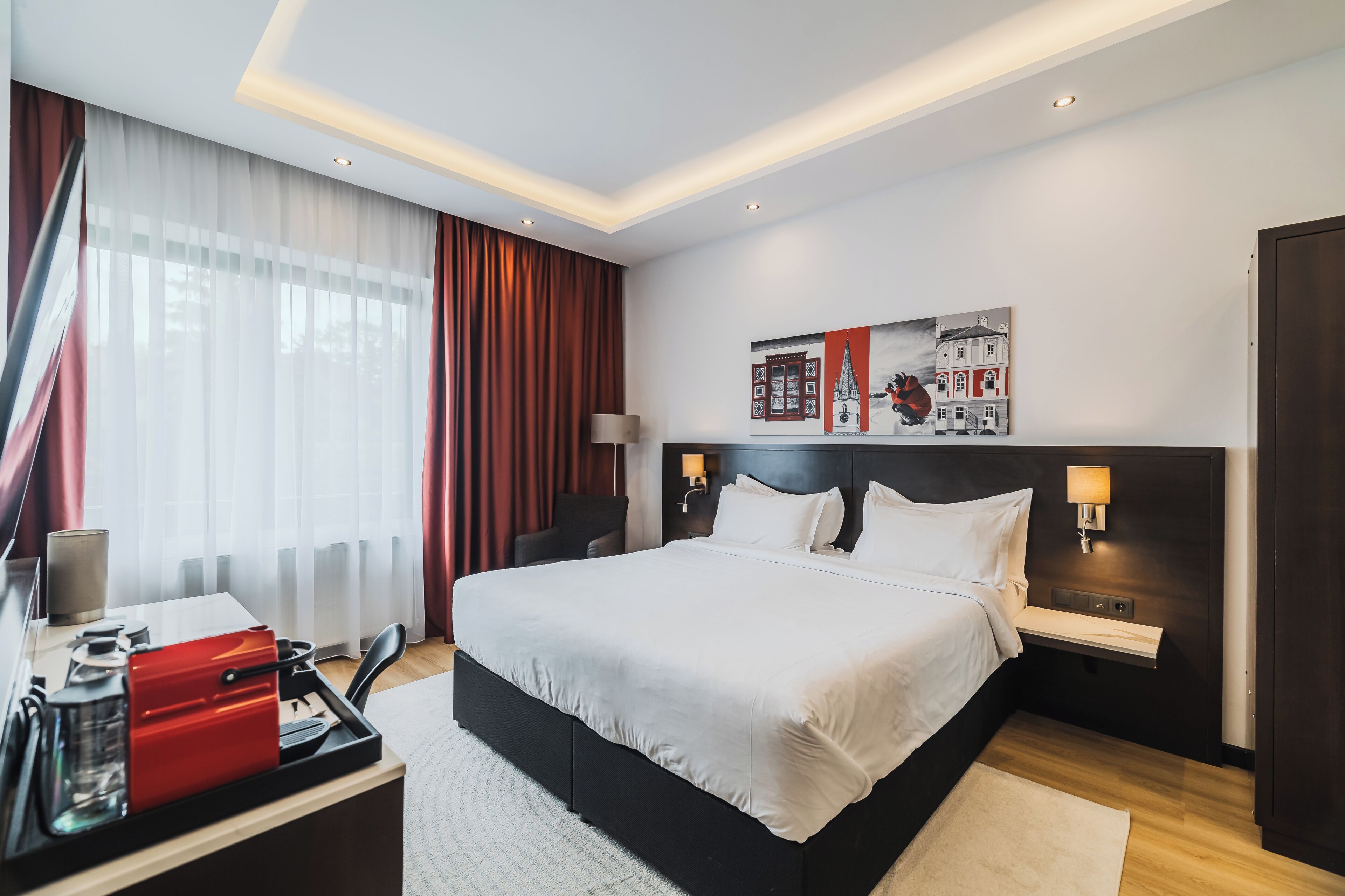 Una camera d'albergo moderna con un letto grande, comodini, una scrivania con un apparecchio rosso e un quadro appeso al muro.