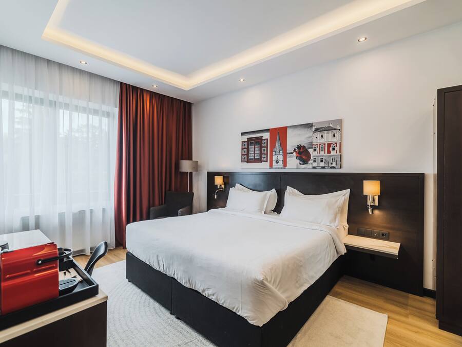 Una camera d'albergo moderna con un letto grande, comodini, una scrivania con un apparecchio rosso e un quadro appeso al muro.