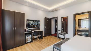 A modern hotel room with a large bed, a desk with a computer, a wardrobe, a mirror with lights, and a TV on the wall.