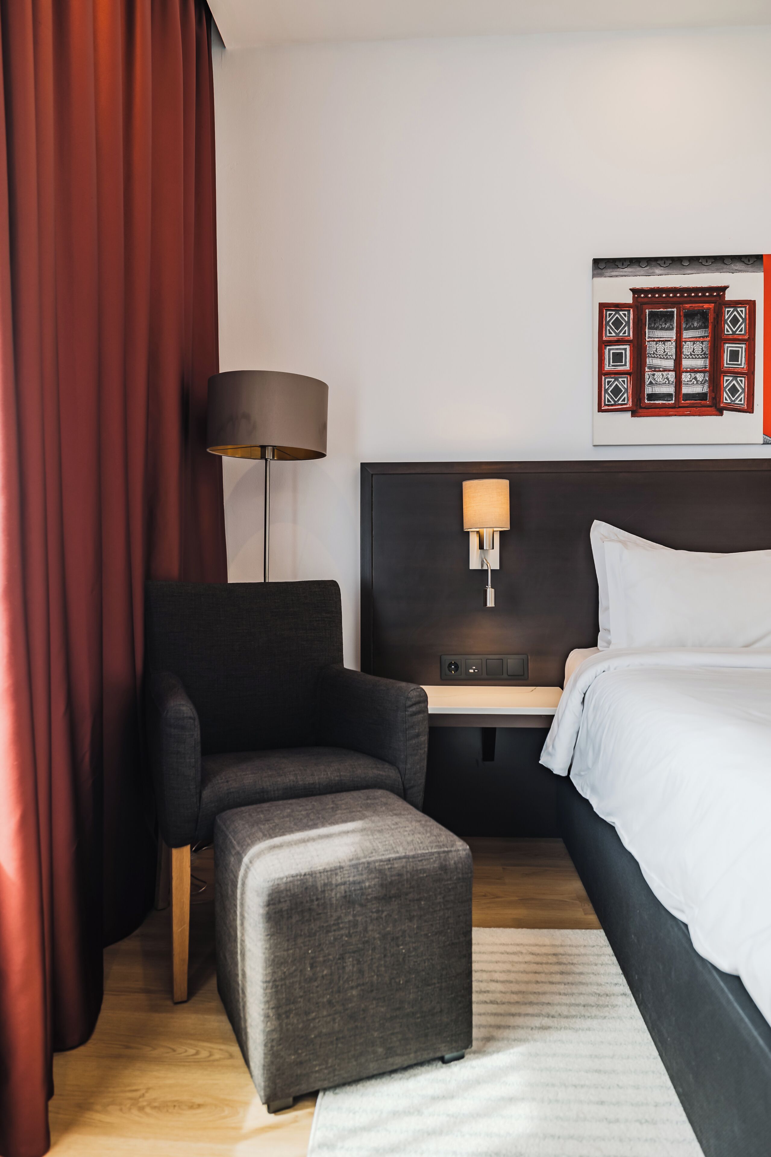 A hotel room with a bed, a desk, a chair, a lamp, and a wall-mounted TV.