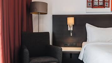 A hotel room with a bed, a desk, a chair, a lamp, and a wall-mounted TV.