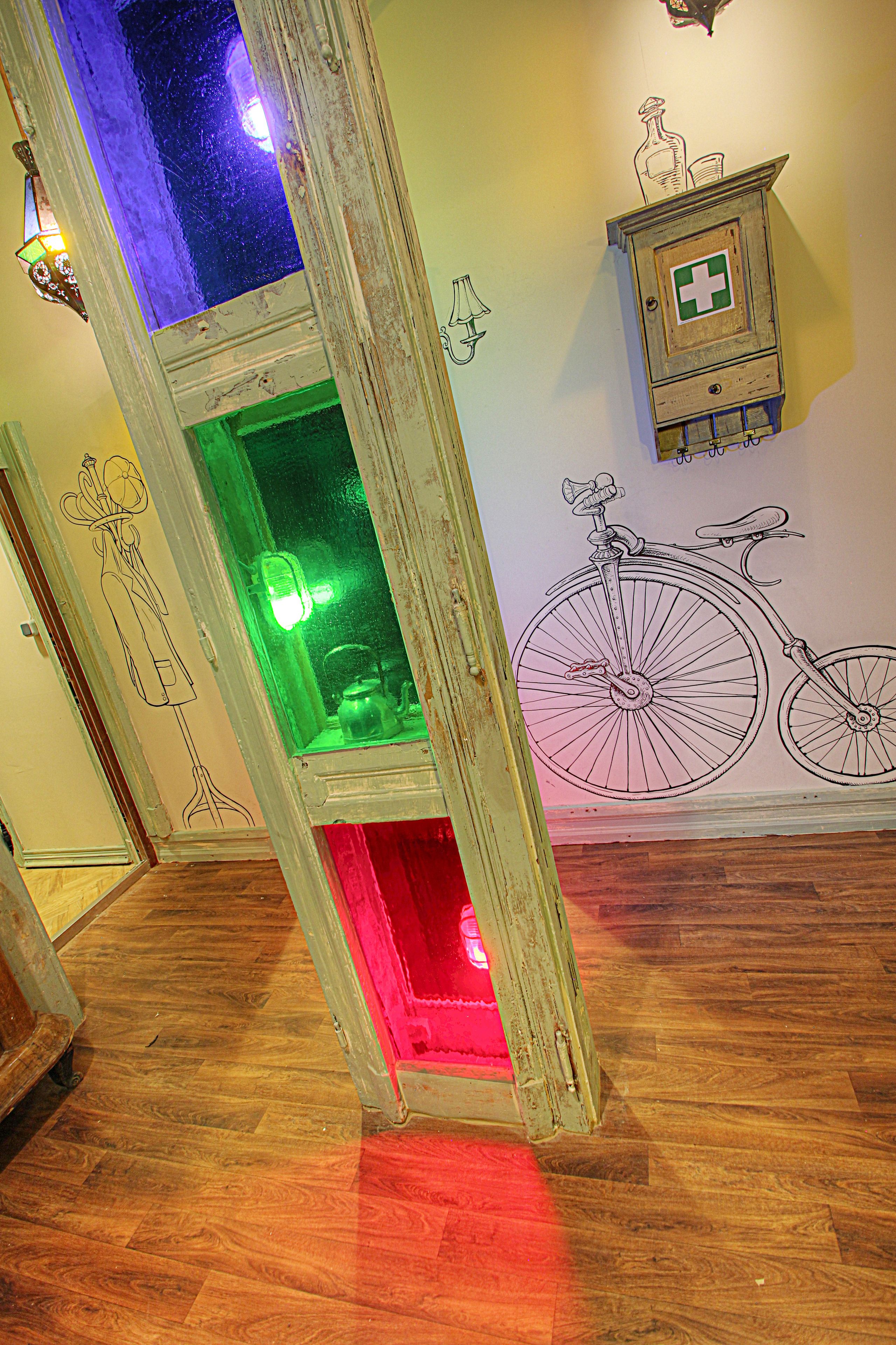 A room with wooden flooring, a wall-mounted cabinet with a medical symbol, and a large wall mural of a bicycle.
