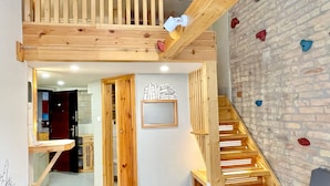 Een houten interieur met een trap, een muur met klimgrepen en een ingelijst kunstwerk aan de wand.