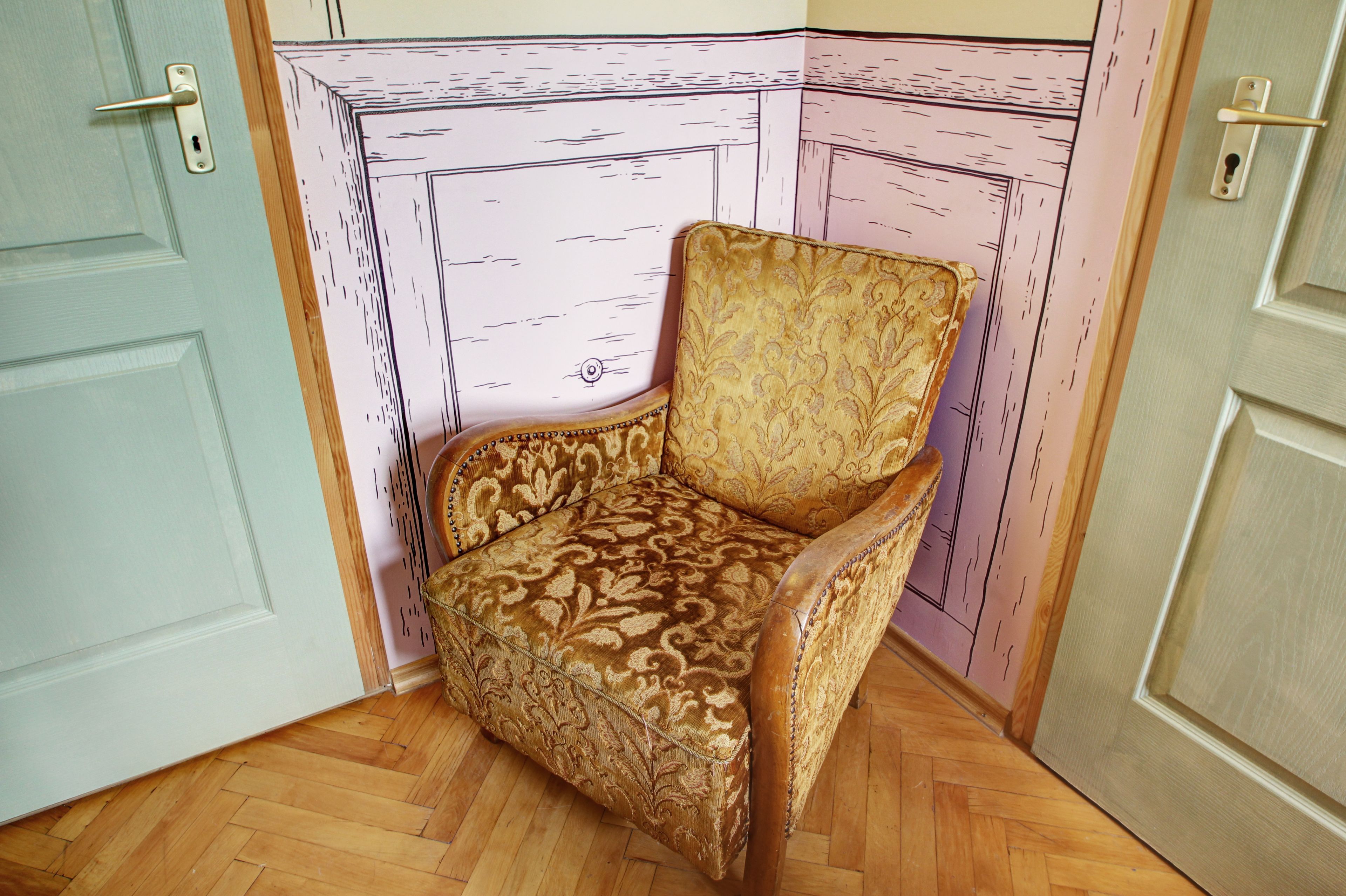 Una habitación de esquina con un sillón estampado, piso de madera y una puerta de diseño sencillo.