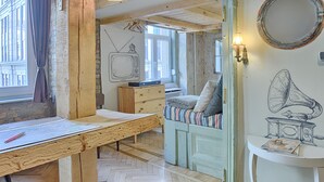 Een kamer met zichtbare houten balken, een houten bureau met een kaart, een bed met gestreepte beddengoed en een muur met een illustratie van een gramofoon.