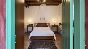 A bedroom with a wooden ceiling, a bed with a white canopy, two bedside tables with lamps, and a patterned rug. - Villa de Loulia Hotel (Corfu)