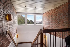 A staircase with brick walls, a wooden railing, and a view of a mountainous landscape through large windows. - Sogn Hotel (Vadheim)