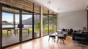 A modern living room with large glass doors, a wooden floor, a sofa, two chairs, and a small table. - Sogn Hotel (Vadheim)