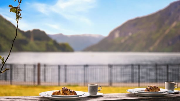 A lakeside view with a wooden deck, two plates of food, and two cups. - Sogn Hotel (Vadheim)
