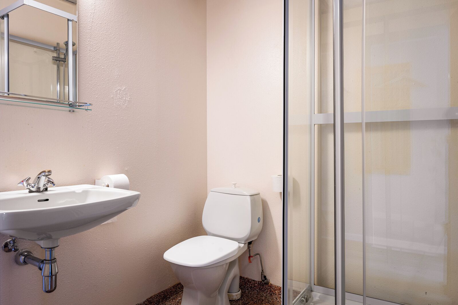 Un baño con lavamanos, inodoro y cabina de ducha con mampara de vidrio.