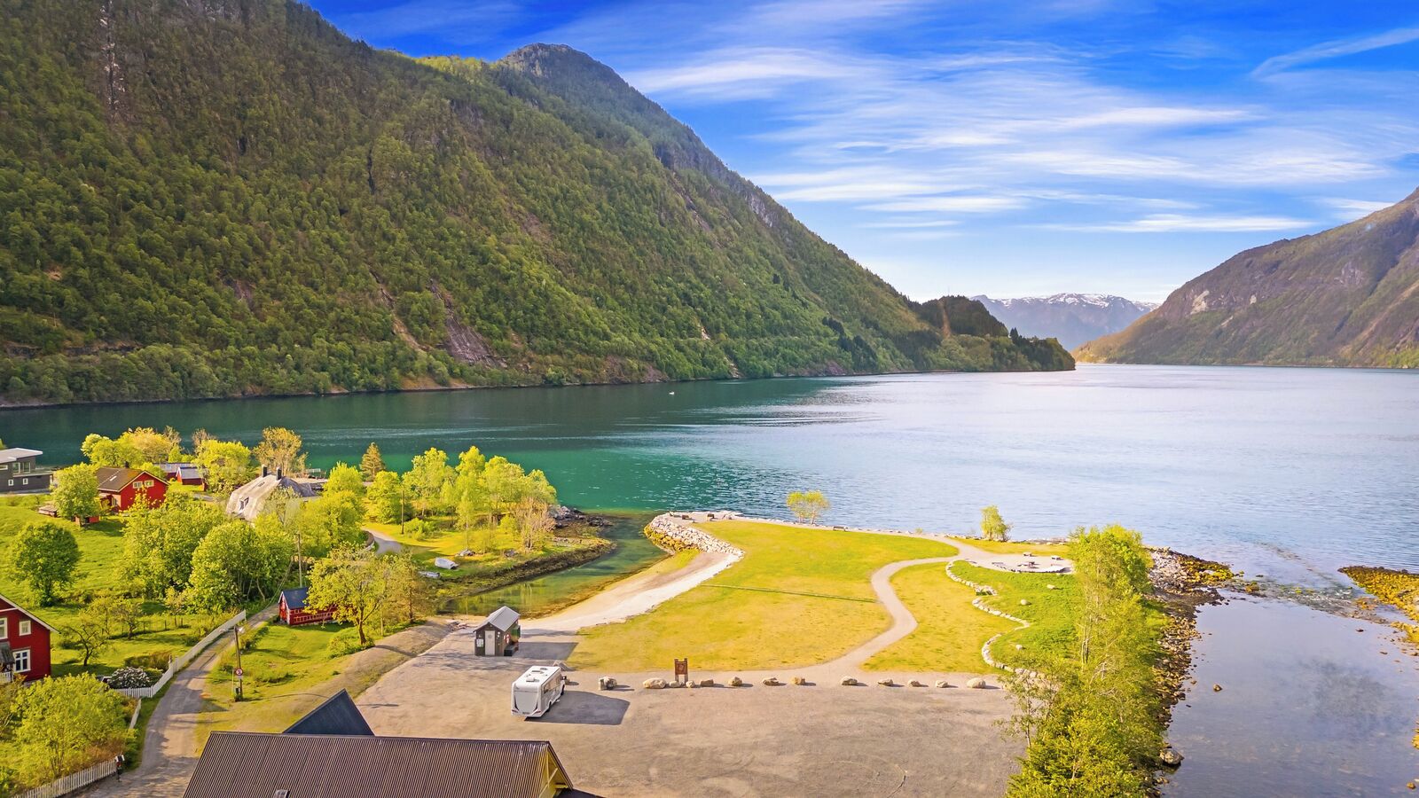 En ejendom ved søen med parkeringsplads, en mindre bygning og et rødt hus.
