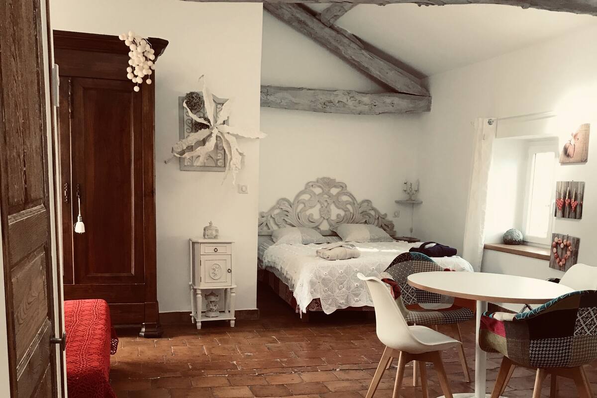 Una habitación acogedora con una cama, una mesa y sillas. Se observa una puerta de madera y una ventana.