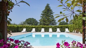 A swimming pool with white lounge chairs arranged around it, surrounded by greenery and a hedge. - Tenuta De Fanti Agriturismo (Bibbona)