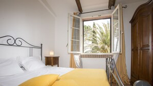 A bed with white and yellow bedding, a nightstand, a wooden wardrobe, and a window with curtains. - Tenuta De Fanti Agriturismo (Bibbona)