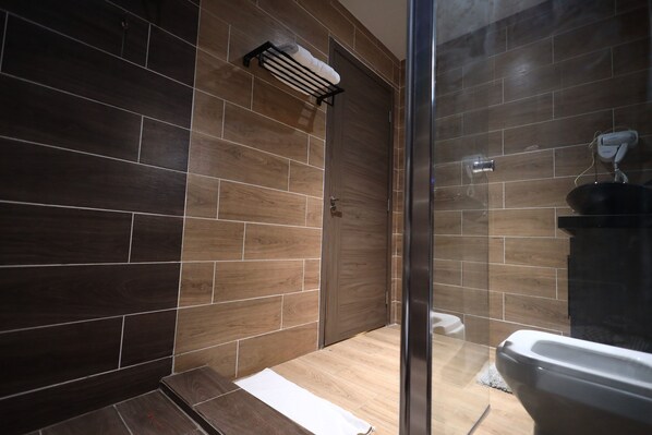 A modern bathroom with dark wood tiles, a glass shower enclosure, and a white sink.