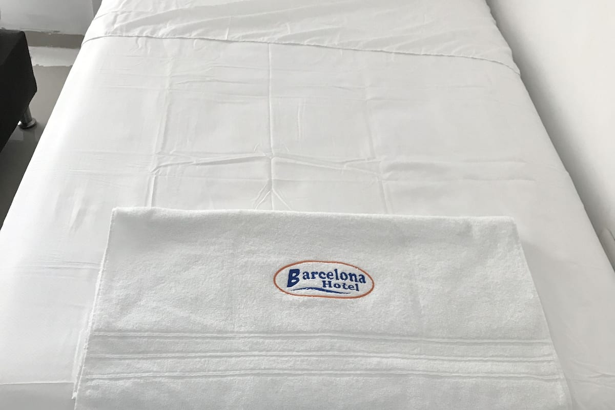 A single bed with a Barcelona Hotel logo on the bedspread.