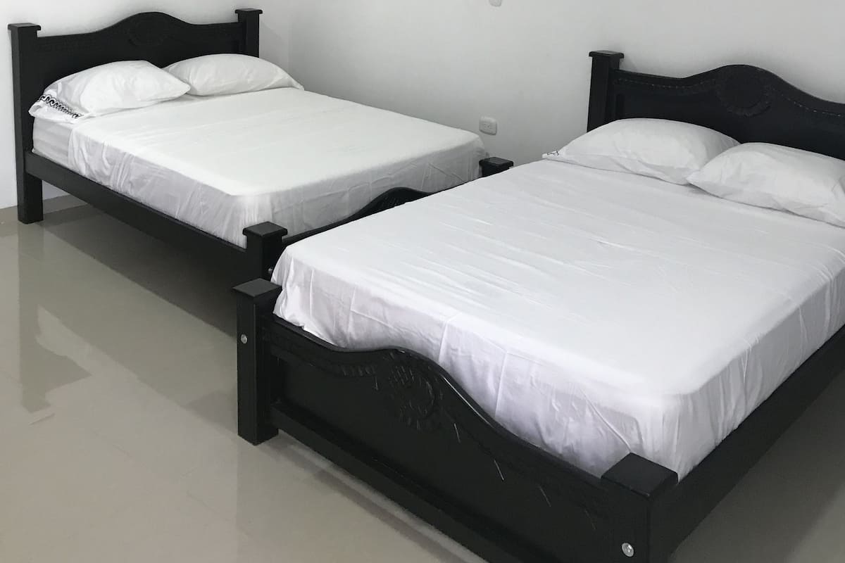 A room with two single beds, a ceiling fan, and an air conditioning unit on the wall.
