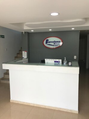 A reception desk with a sign for Barcelona Hotel, a glass partition, and a staircase in the background. - Barcelona Hotel (Montería)